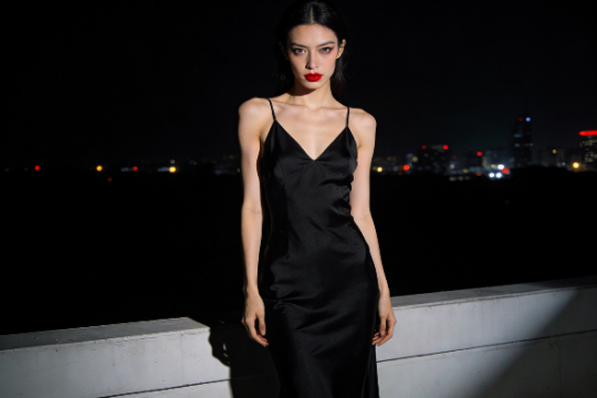 Elegant woman in black dress with red lipstick against a city nightscape.
